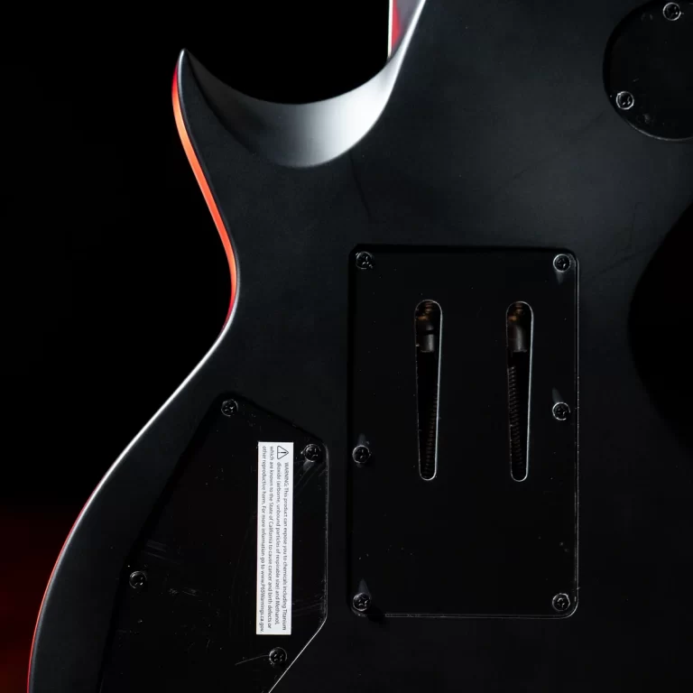 Back of a black electric guitar showing the rear cavity plate with two vertical slots and red edge outline, low lighting. ขายราคาพิเศษ
