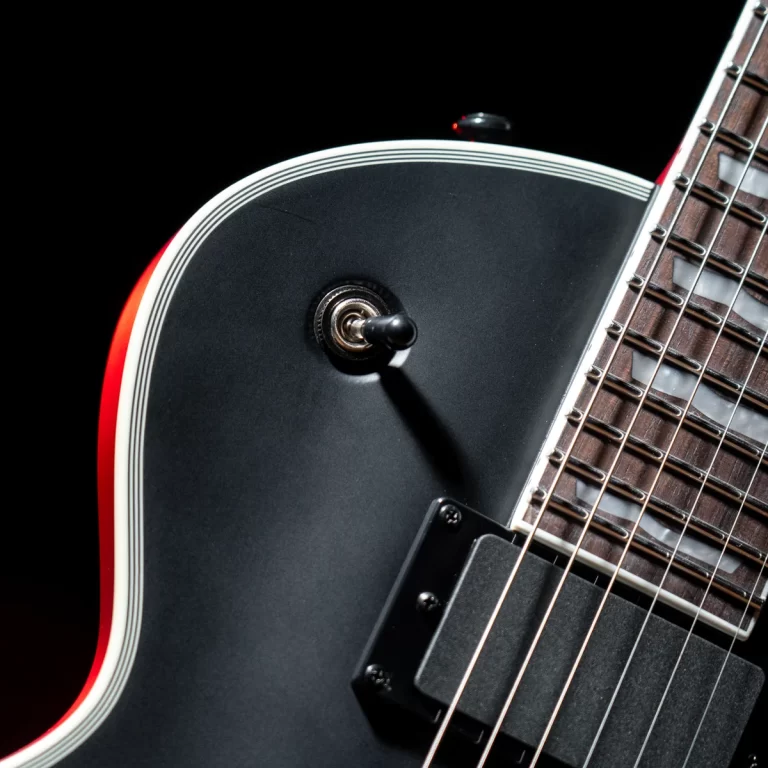 Close-up of a dark electric guitar body showing a chrome toggle switch, white binding, and part of the fretboard and pickup against a black background. ขายราคาพิเศษ