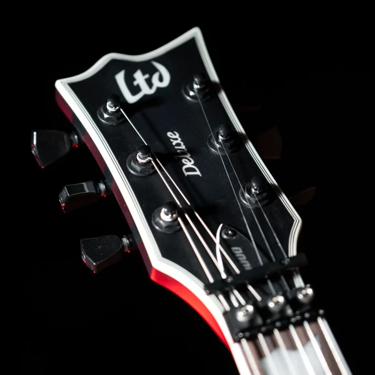 Close-up of a black LTD Deluxe guitar headstock with six tuning pegs and strings against a dark background. ขายราคาพิเศษ