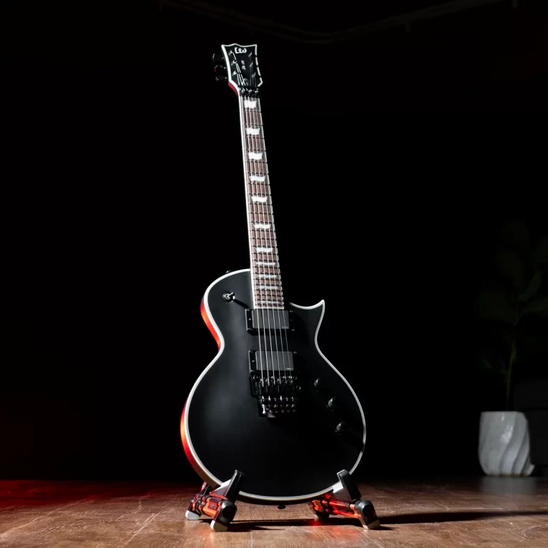 Black electric guitar on a stand, on a dimly lit stage with red-tinged edges. 1- or single-cutaway body with chrome hardware. ขายราคาพิเศษ