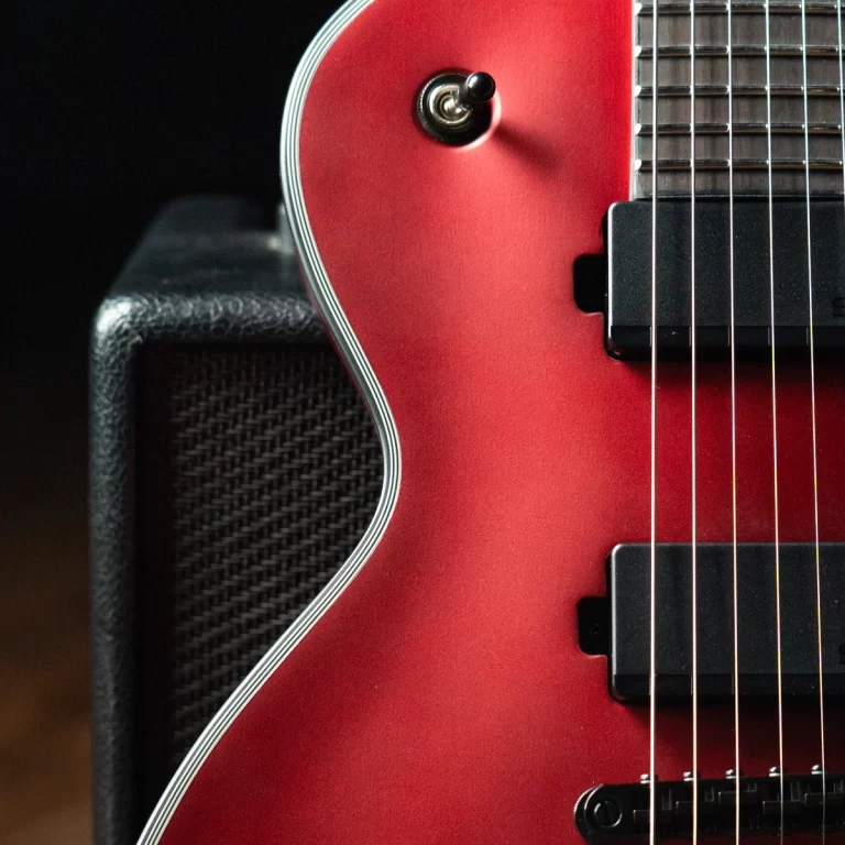 Close-up of a red electric guitar body with chrome binding, two black pickups, and strings over the pickups ขายราคาพิเศษ