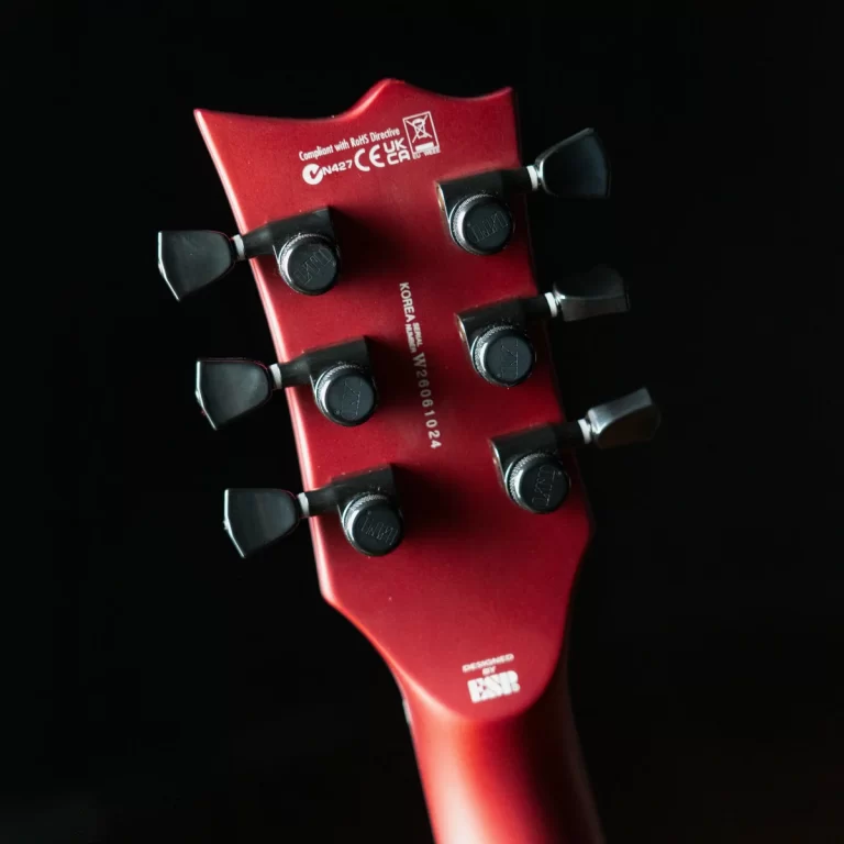 Close-up of a red guitar headstock with six black tuning pegs against a black background, showing part of the neck. ขายราคาพิเศษ