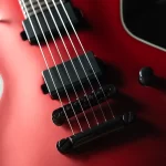 Close-up of a red electric guitar showing strings, pickups, and bridge on a glossy finish surface, emphasizing the instrument's hardware. ขายราคาพิเศษ