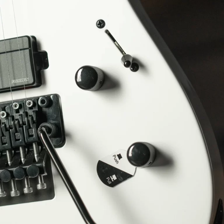 Close-up of a white electric guitar's bridge area with knobs and loose screws on the body, a small tool nearby, indicating a setup or repair scene. ขายราคาพิเศษ