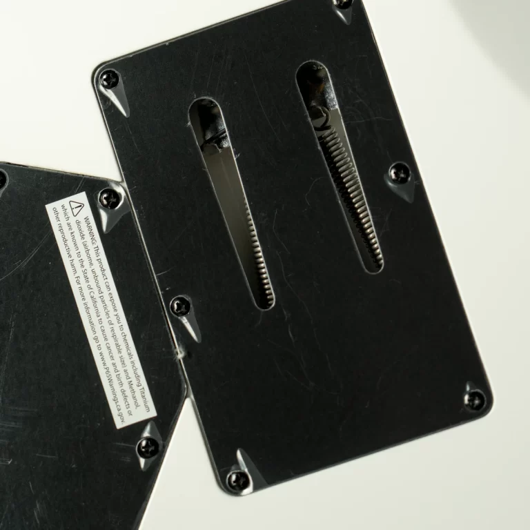 Close-up of a black metal panel with two vertical slots and exposed springs, screws at corners, and a warning label visible. ขายราคาพิเศษ