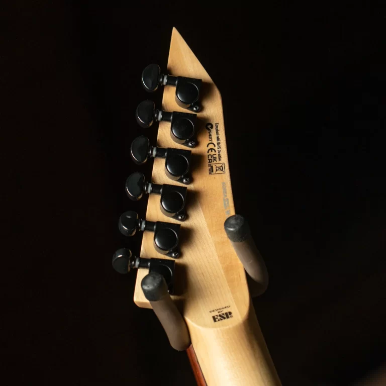 Close-up of a light-wood guitar headstock with black tuning pegs arranged along the side, set against a dark background ขายราคาพิเศษ