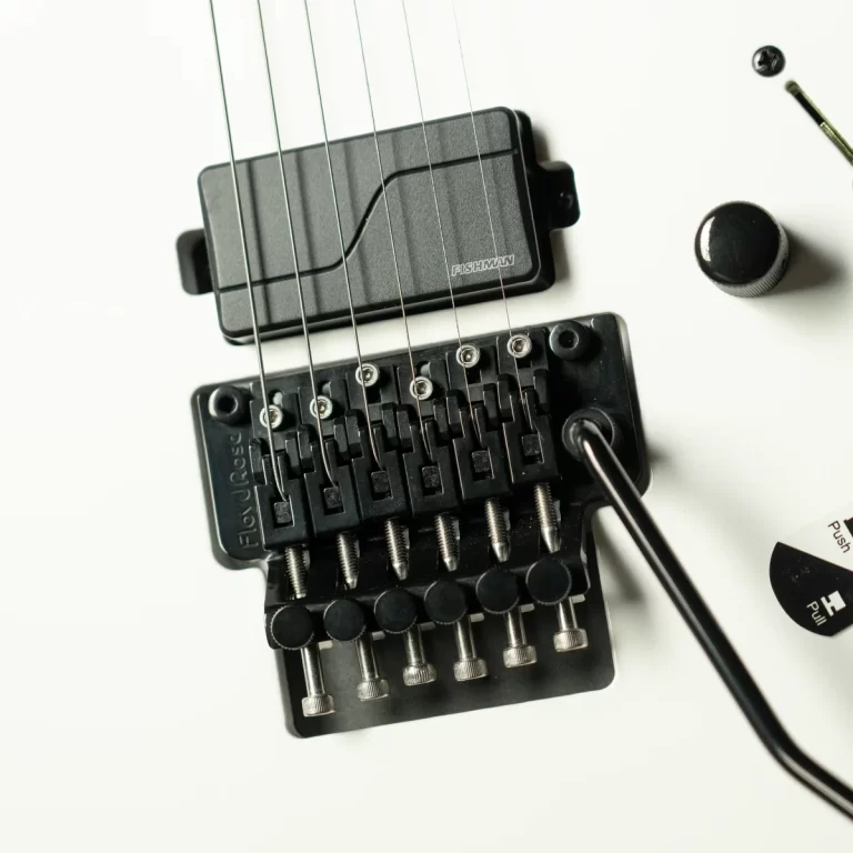 Close-up of a guitar bridge with a Fishman pickup plate and six strings resting above the saddles on a white surface. ขายราคาพิเศษ