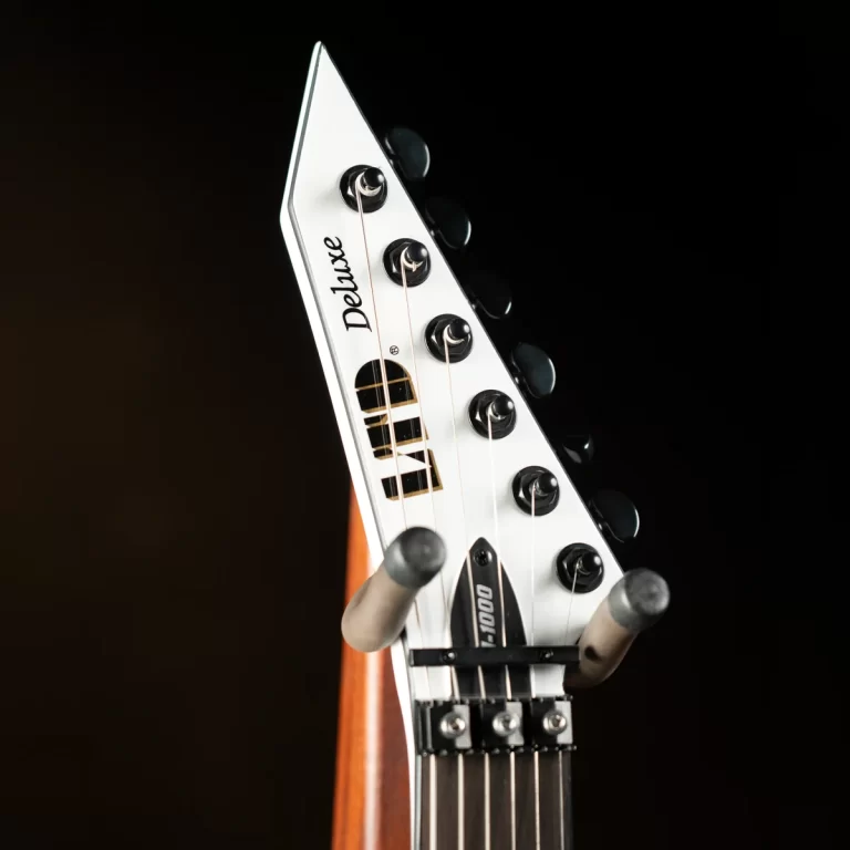 Close-up of a white electric guitar headstock labeled 'Deluxe' with tuning pegs and strings against a dark background. ขายราคาพิเศษ