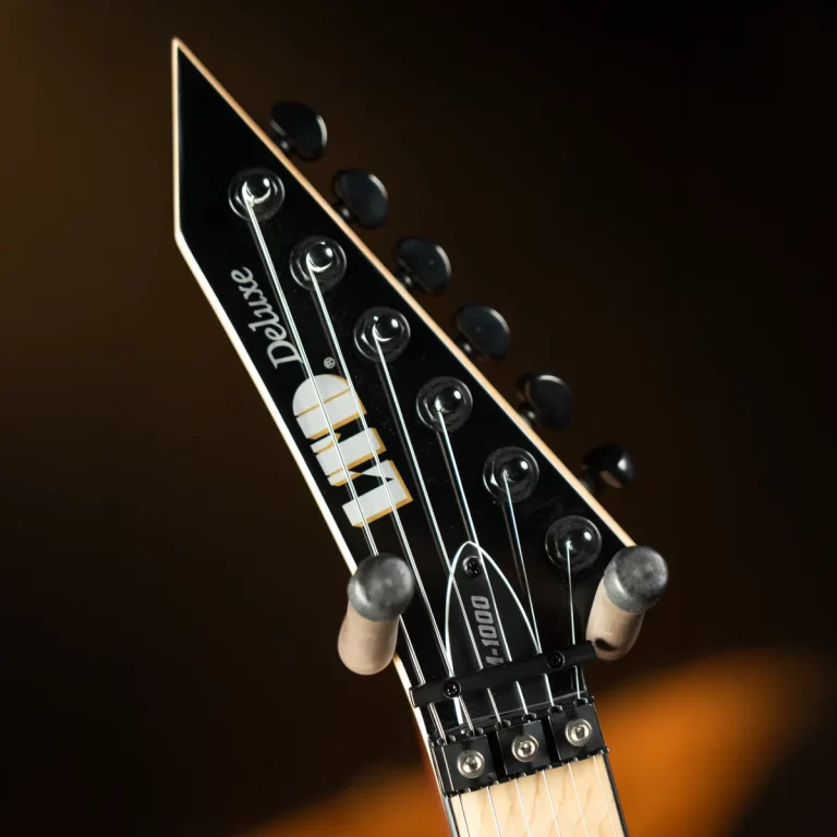 Close-up of a black electric guitar headstock with six tuning pegs and strings against a dark background ขายราคาพิเศษ