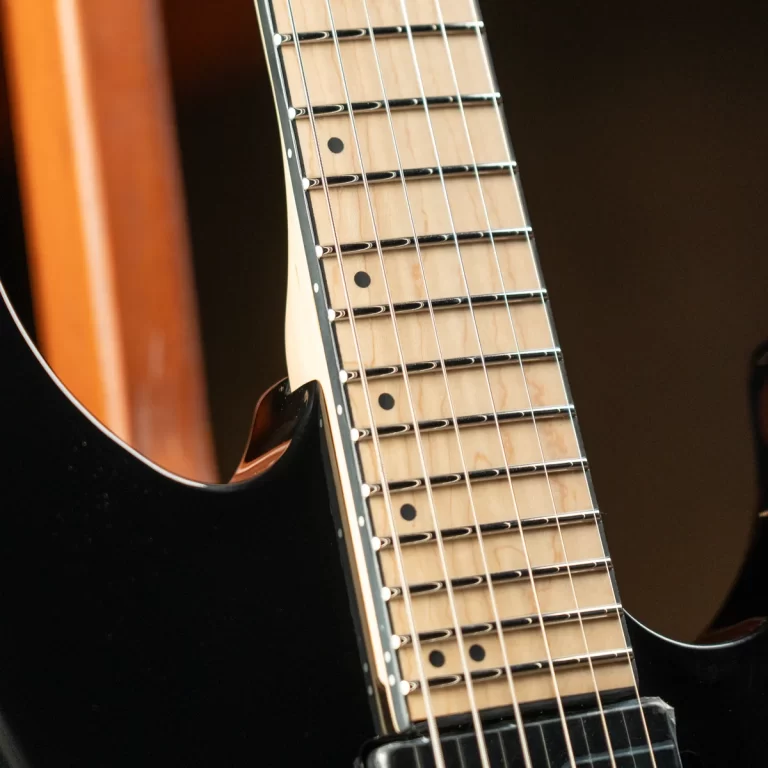 Close-up of a guitar neck showing frets and strings along a maple fingerboard on a dark body, partial orange edge visible ขายราคาพิเศษ