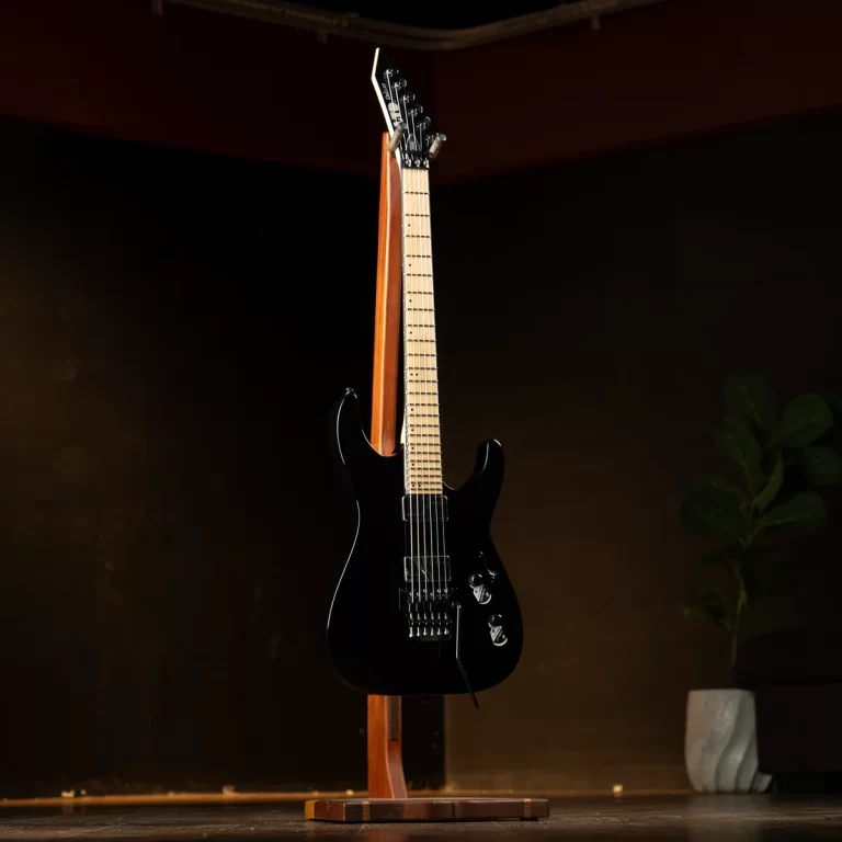 Black electric guitar on a wooden stand in a dimly lit stage setting. ขายราคาพิเศษ