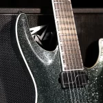 Close-up of a glittery dark-green electric guitar body with neck and pickup visible against a textured black background. ขายราคาพิเศษ