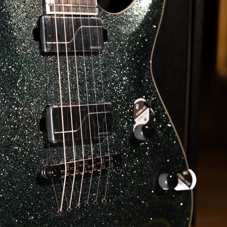 Close-up of a dark, glittery green electric guitar body showing two black humbucker pickups, strings, and a bridge. ขายราคาพิเศษ