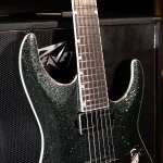 Glittery dark-green electric guitar resting against a large black amplifier, close-up of neck and strings visible. ขายราคาพิเศษ