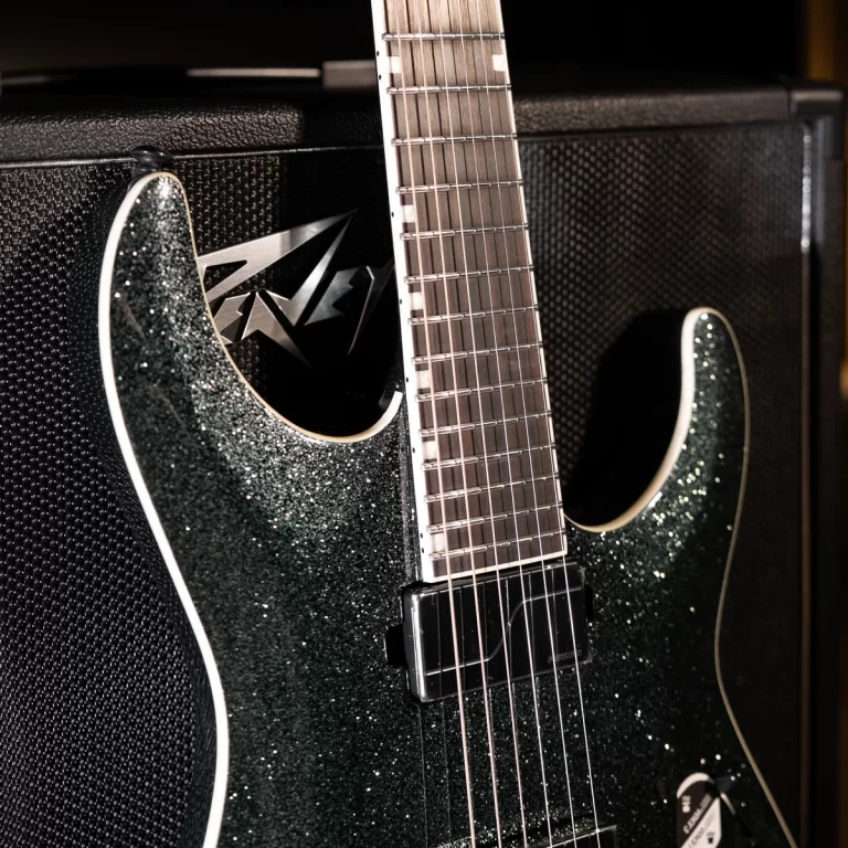Glittery dark-green electric guitar resting against a large black amplifier, close-up of neck and strings visible. ขายราคาพิเศษ