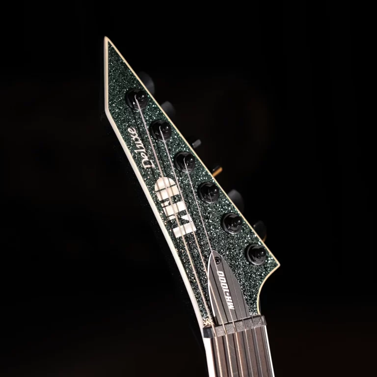 Close-up of a glittery green electric guitar headstock with six tuning pegs and strings against a dark background. ขายราคาพิเศษ