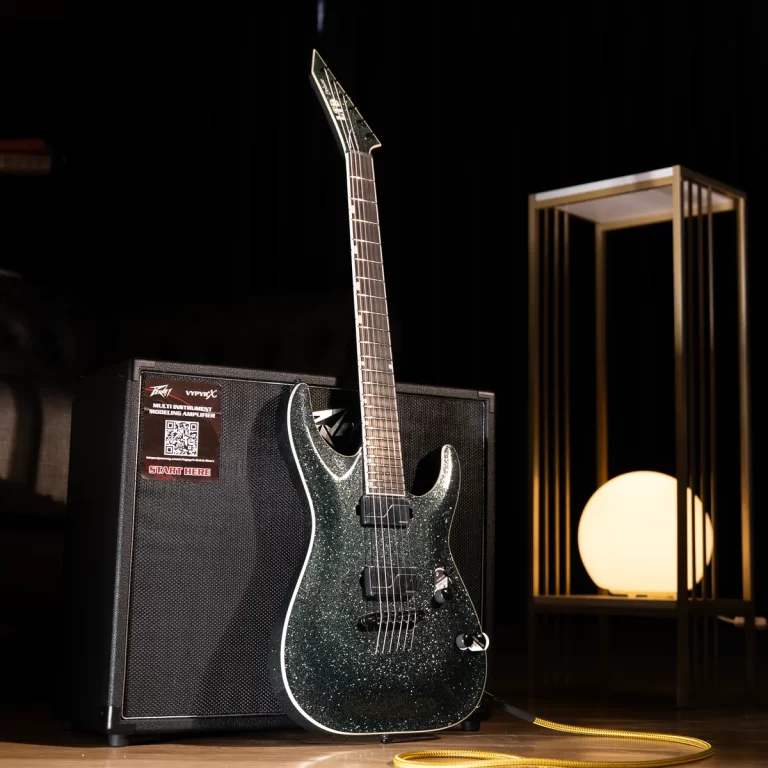 Sparkly dark green electric guitar resting on a black amplifier with a yellow instrument cable, set on a dark stage. ขายราคาพิเศษ