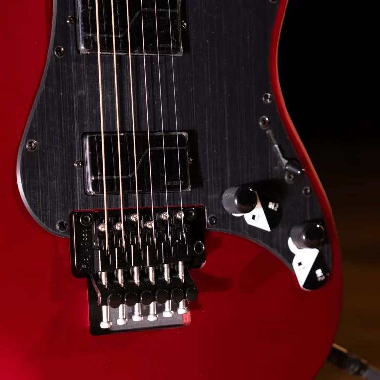 Red electric guitar close-up showing black pickguard, two pickups, and a tremolo bridge with chrome saddles. ขายราคาพิเศษ