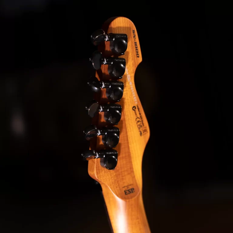 Close-up of a wooden guitar headstock with black tuning pegs against a dark background, showing the neck and hardware in warm lighting. ขายราคาพิเศษ