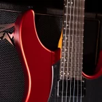 Red electric guitar with a maple neck leaning against a black amplifier. ขายราคาพิเศษ