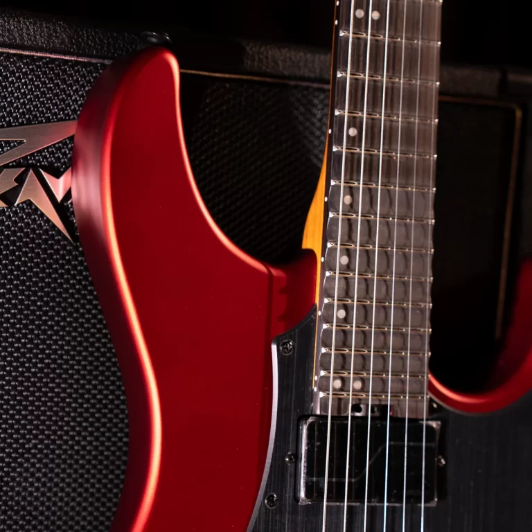 Red electric guitar with a maple neck leaning against a black amplifier. ขายราคาพิเศษ