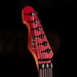 Close-up of a red electric guitar headstock with six tuning pegs and strings against a dark background. ขายราคาพิเศษ