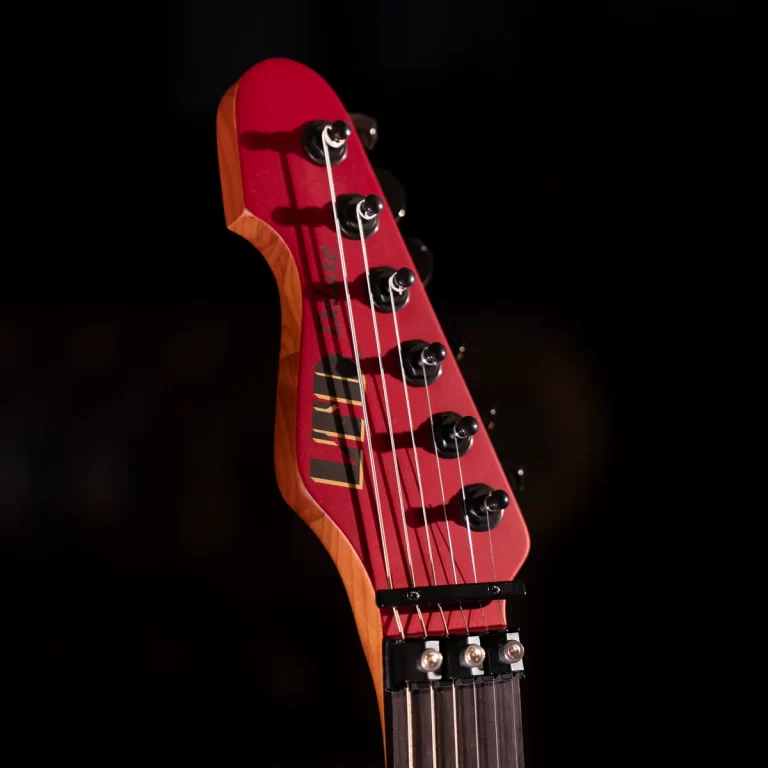 Close-up of a red electric guitar headstock with six tuning pegs and strings against a dark background. ขายราคาพิเศษ