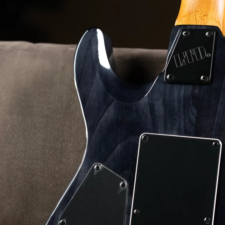 Back of a blue-black electric guitar body with chrome screws and black control plates, resting on a sofa ขายราคาพิเศษ