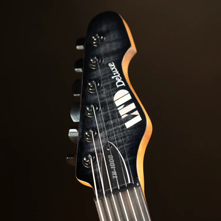 Close-up of a dark guitar headstock with six tuning pegs and strings, angled against a dark background. ขายราคาพิเศษ