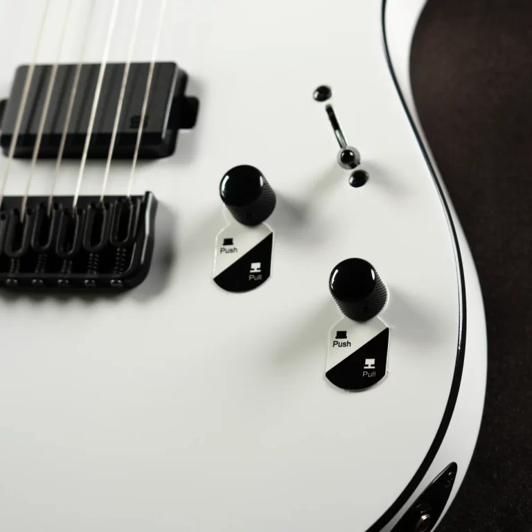 Close-up of a white electric guitar showing two black-knob controls, a pickup, and a tremolo bridge with a pull/push toggle label nearby. ขายราคาพิเศษ