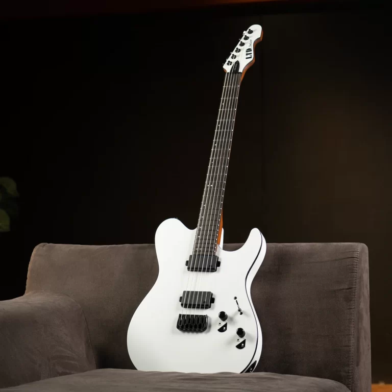 White electric guitar with black pickups and a maple neck resting on a brown sofa against a dark background. ขายราคาพิเศษ
