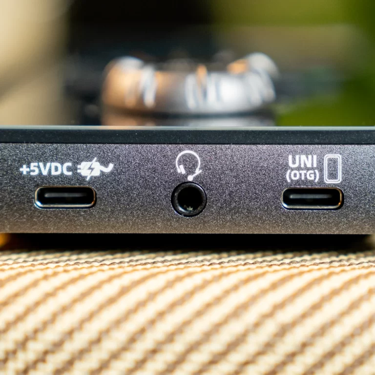 Close-up of a black USB-C hub showing left and right USB-C ports, a center 3.5mm audio jack, and labels +5VDC and UNI (OTG) on a textured surface. ขายราคาพิเศษ