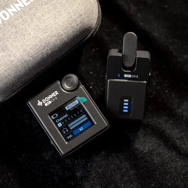 Donner CV‑3 wireless guitar receiver with LCD showing channel, beside the TX transmitter with blue LEDs, on a dark surface beside a case. ขายราคาพิเศษ