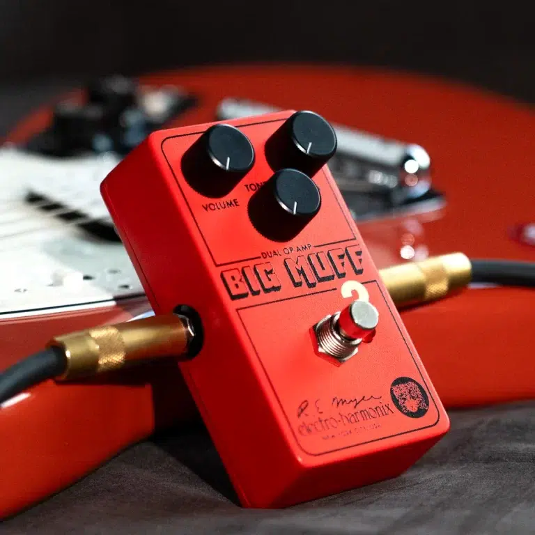 Close-up of a red guitar effects pedal with three black knobs and a footswitch, connected by gold cables on a guitar body edge, labeled 'BLUE WOLF' dual op-amp. ขายราคาพิเศษ