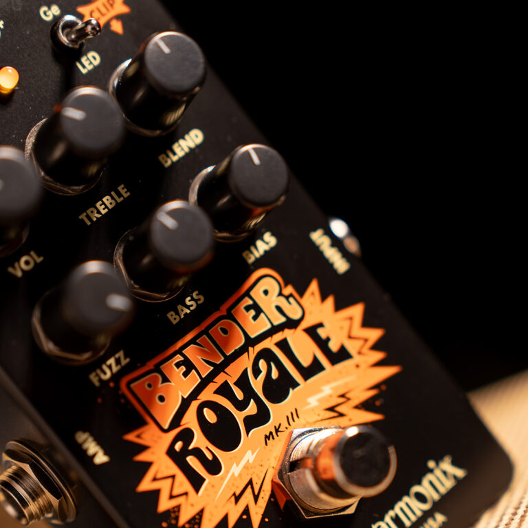 Close-up of a black guitar effects pedal with an orange graphic and multiple knobs labeled Fuzz, Bass, Treble and Volume; the scene is angled against a dark background. ขายราคาพิเศษ