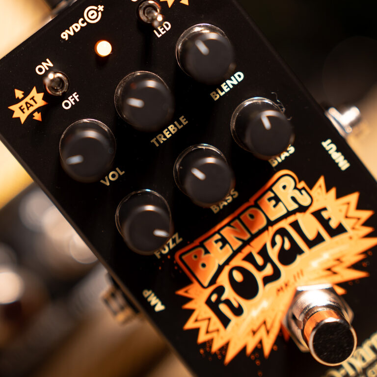 Close-up of a black guitar effects pedal with orange artwork and several knobs labeled VOL, TREBLE, BASS, and MIDS/FX knobs visible. ขายราคาพิเศษ