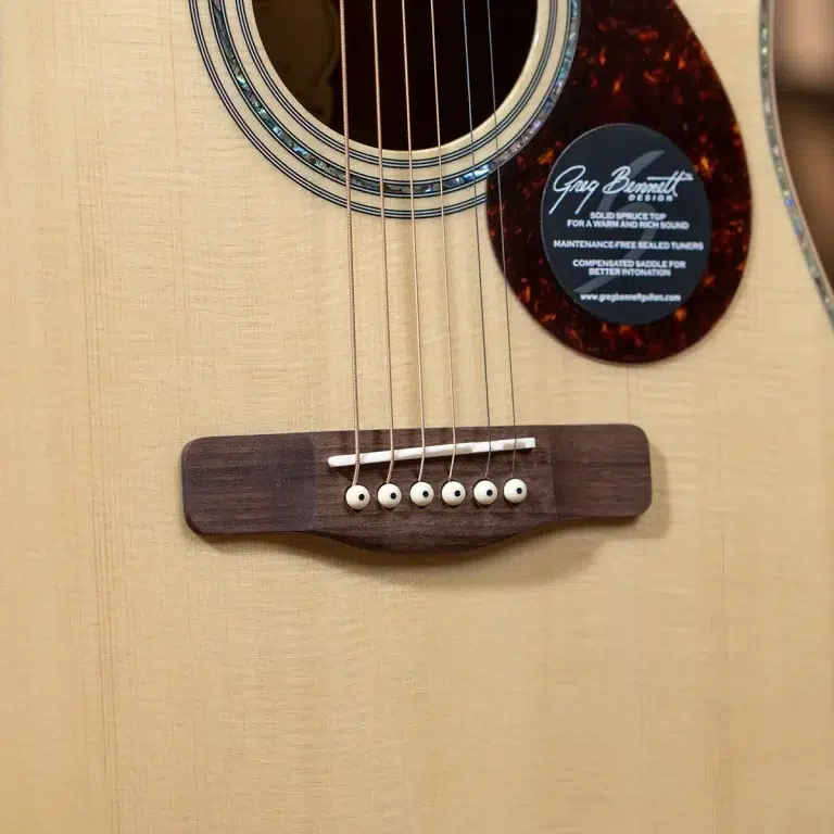 Close-up of an acoustic guitar body with six strings anchored at the wooden bridge and a circular tortoiseshell pickguard near the strings. ขายราคาพิเศษ