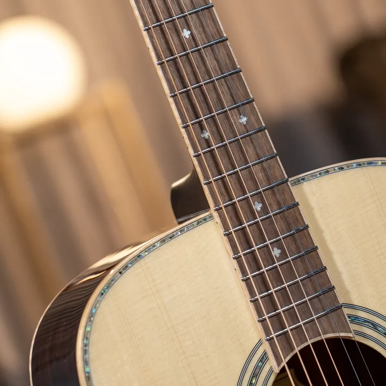 Close-up of an acoustic guitar neck and fretboard with strings and inlay dots, warm lighting in the background ขายราคาพิเศษ