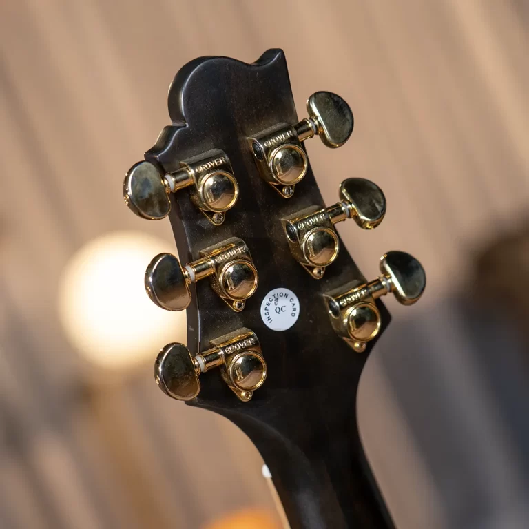 Close-up of a black guitar headstock showing gold tuning pegs and a white QC sticker on the back. ขายราคาพิเศษ