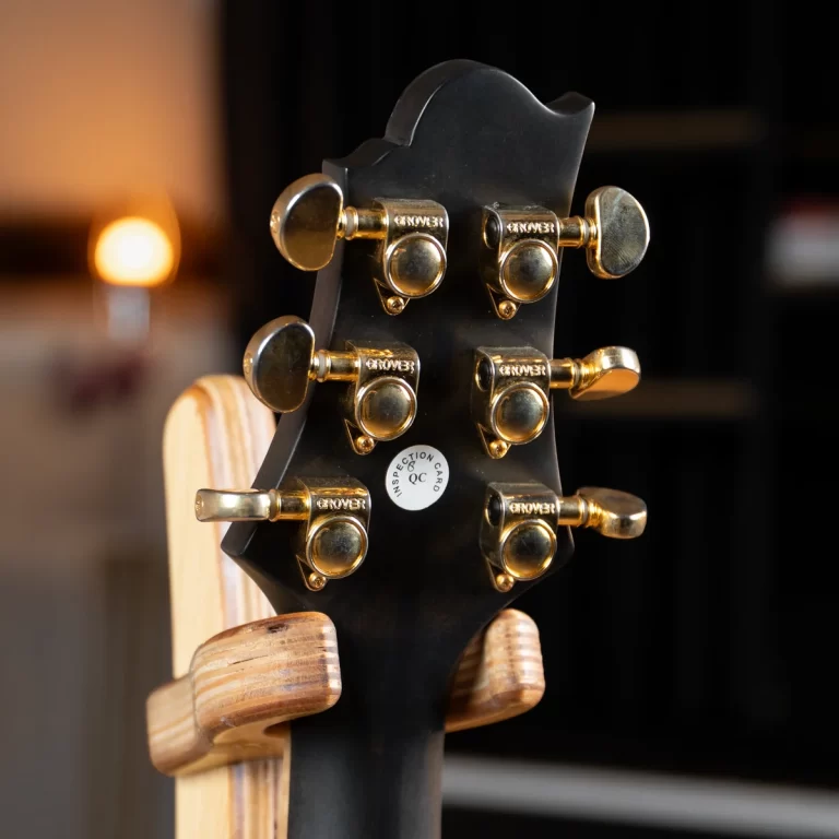 Back of a black guitar headstock with gold Grover tuning pegs and a small QC sticker visible on the back. ขายราคาพิเศษ