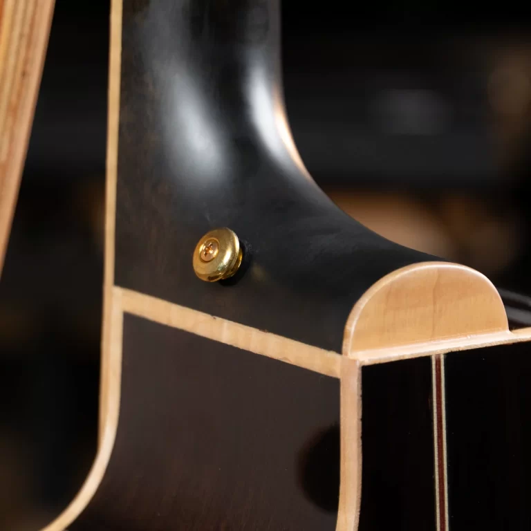 Close-up of a black guitar body with a brass strap button near the neck joint and light wood binding detail ขายราคาพิเศษ