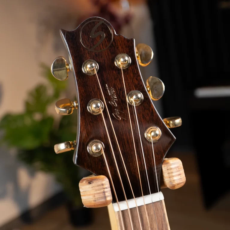 Close-up of a wooden guitar headstock with gold tuning pegs and strings running down the neck ขายราคาพิเศษ