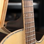 Close-up of a guitar neck and fretboard with metal frets and strings against a dark background ขายราคาพิเศษ