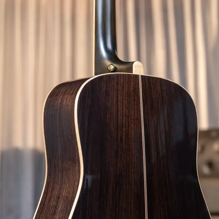 Close-up of a dark wooden guitar back, showing cream binding along the edge and the neck joint at the top stump. ขายราคาพิเศษ