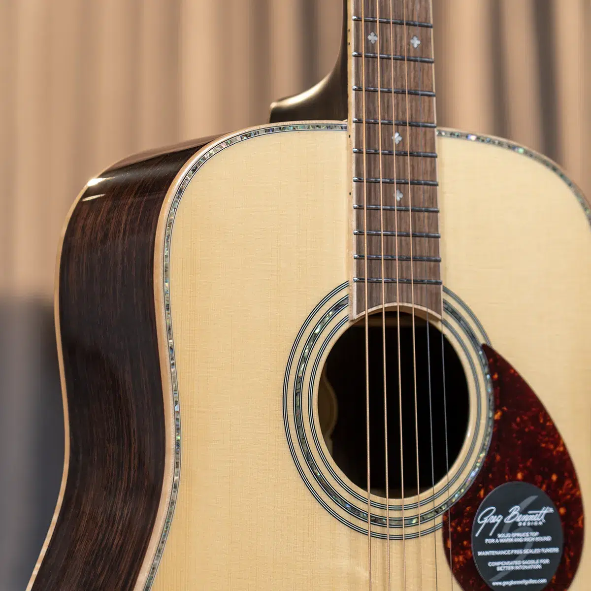 Close-up of an acoustic guitar body: light top, dark back, decorative rosette around the sound hole, and strings across the fretboard above the hole.