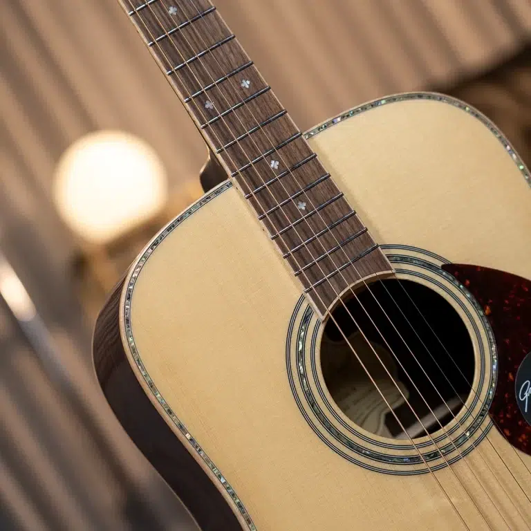 Close-up of an acoustic guitar's fretboard and soundhole, showing metal frets and inlay dots against a warm wood background. ขายราคาพิเศษ