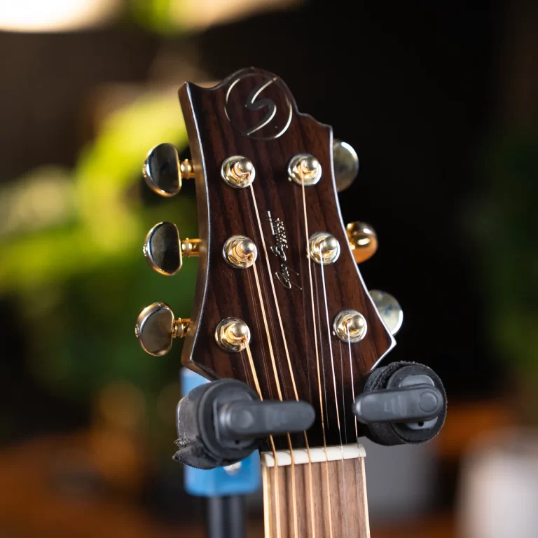 Close-up of a dark wooden guitar headstock with six gold tuning pegs and strings. ขายราคาพิเศษ