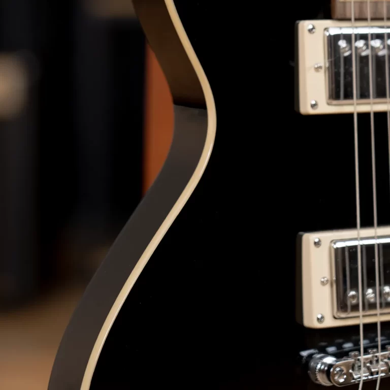 Close-up of a black electric guitar body with cream binding and chrome hardware along the edge and pickups at the right ขายราคาพิเศษ