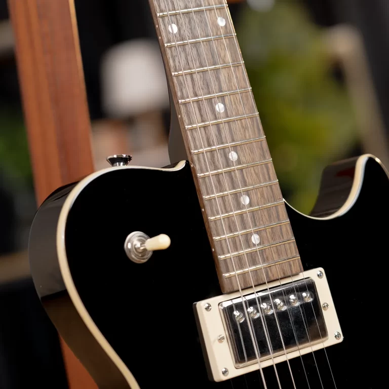 Close-up of a black electric guitar neck and body, showing the fretboard with dot inlays and a cream pickup nearby. ขายราคาพิเศษ