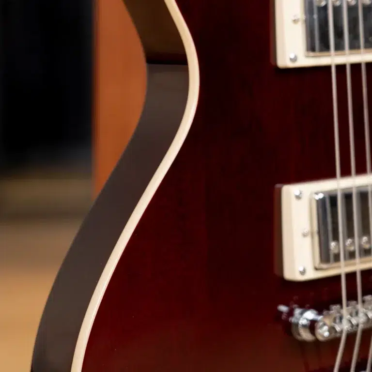 Close-up of a burgundy electric guitar body edge with white binding and chrome pickups visible on the rightside of the frame. ขายราคาพิเศษ